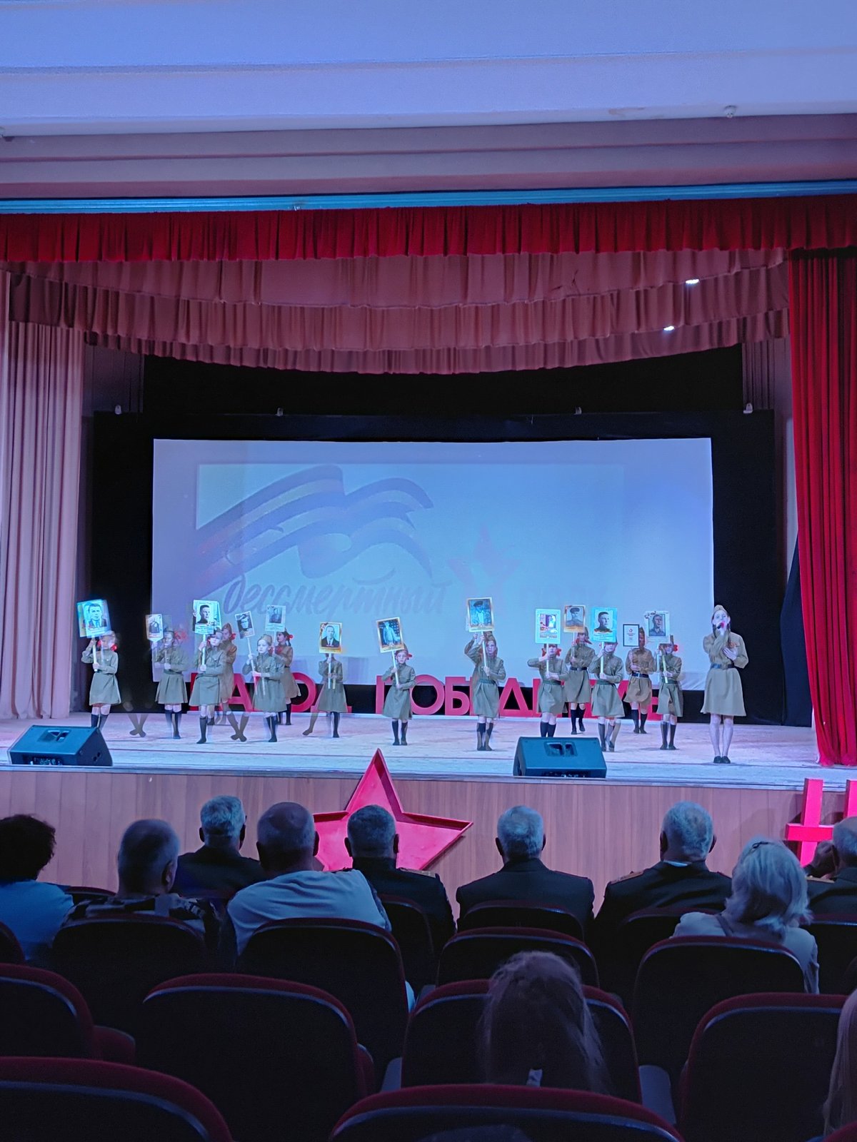 Children perform commemorative theater presentation with framed pictures