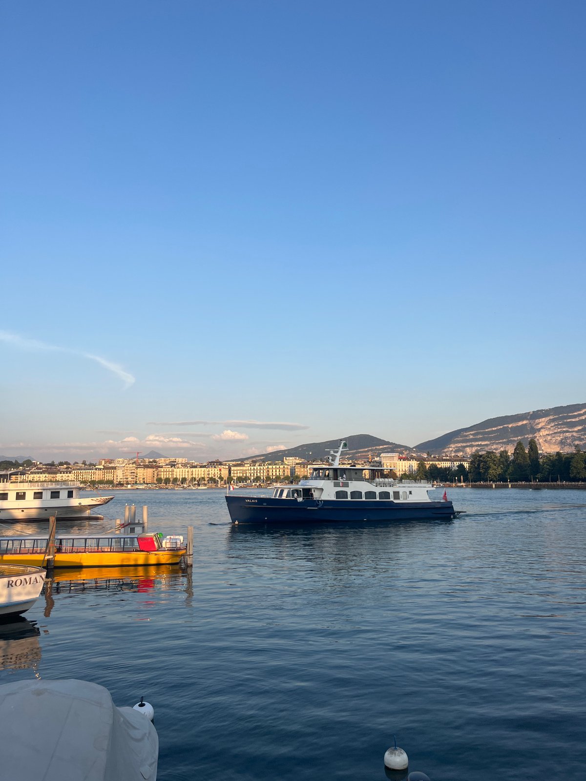 Geneva lakefront at dusk: boats, the Brunswick Monument, and street scenes.