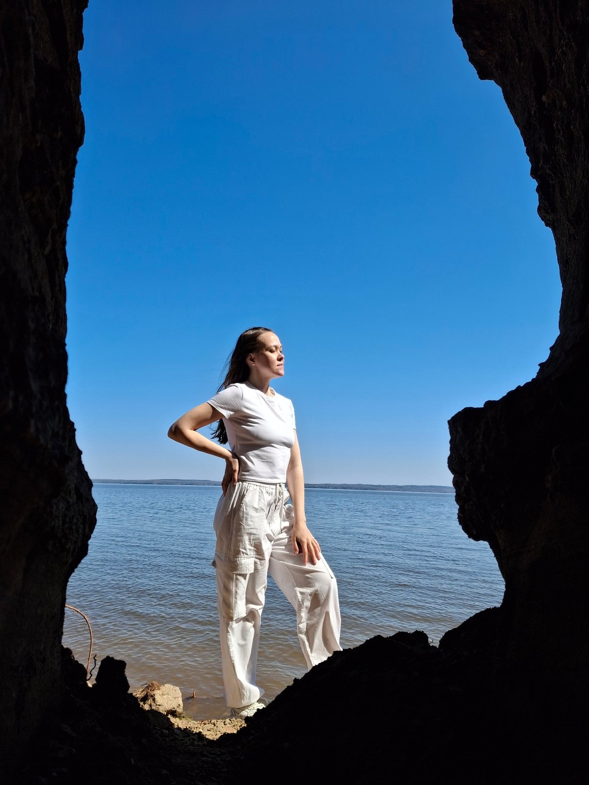 Woman stands at cave entrance overlooking water and sky