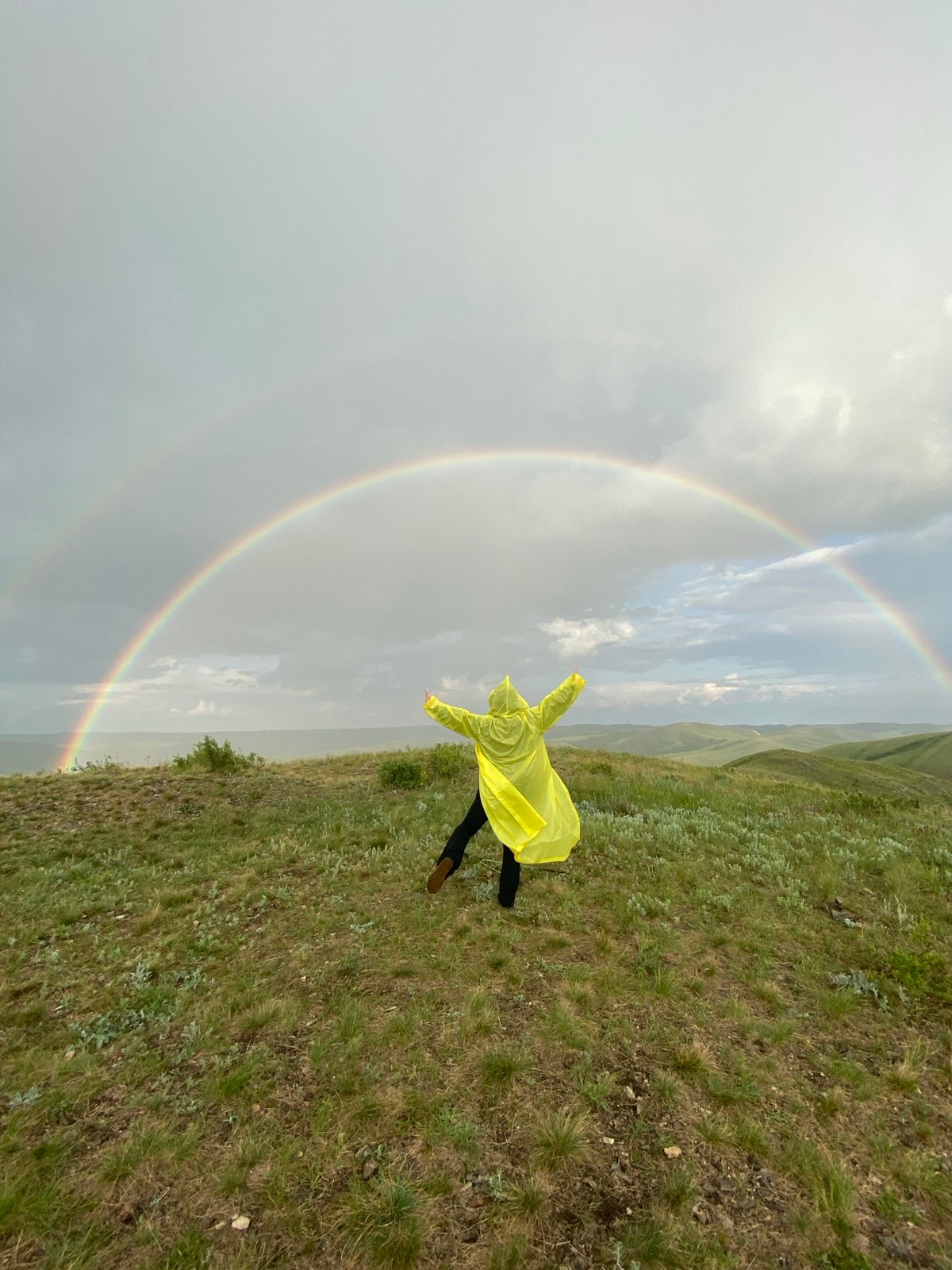 Person celebrates double rainbow on Russian hillside