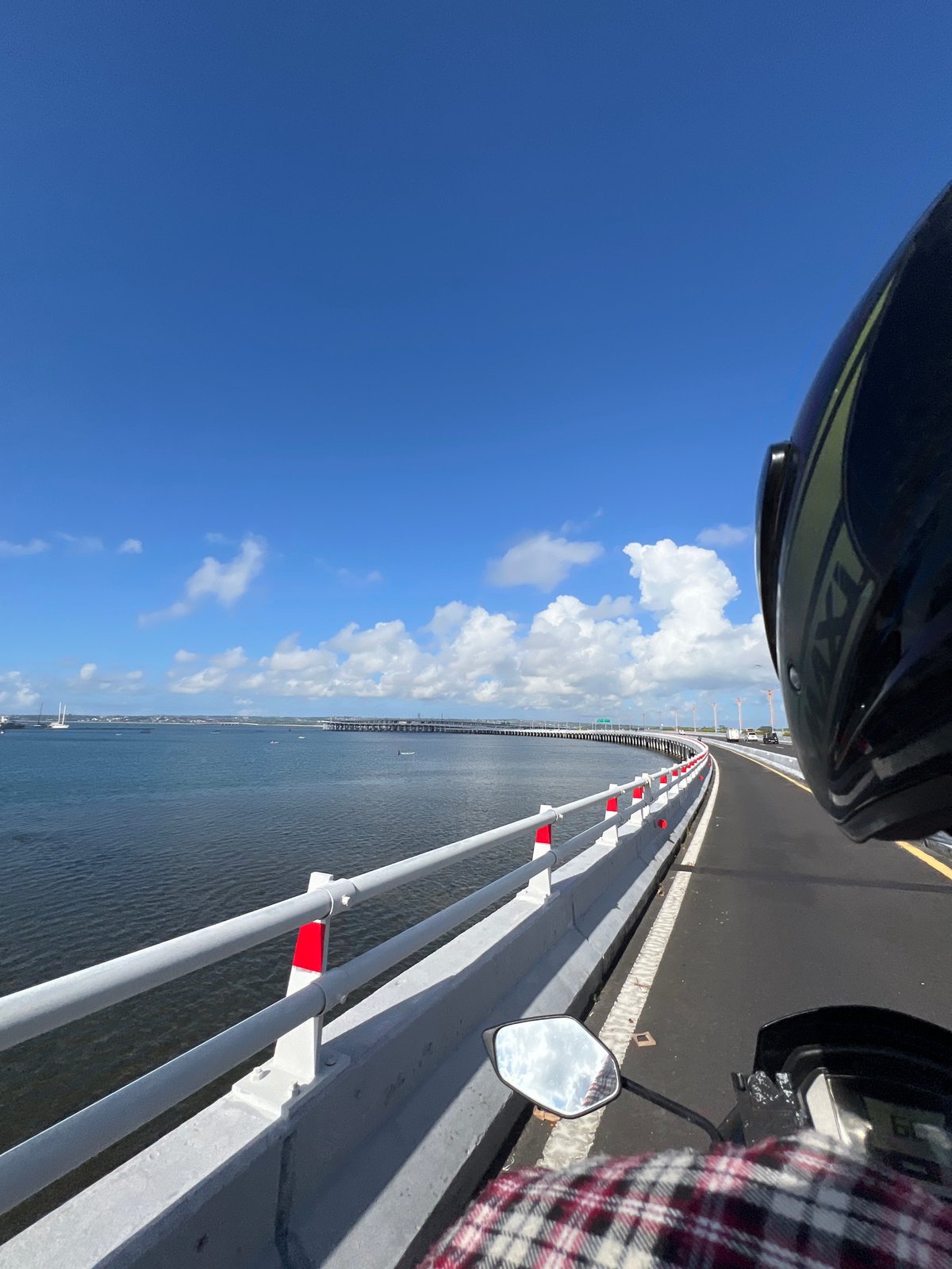 Motorcyclist crosses bridge as paddleboarder navigates waterway below in Kuta