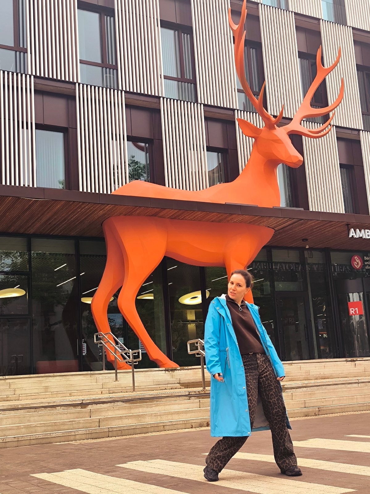 Woman photographed at Riga building with orange deer sculpture