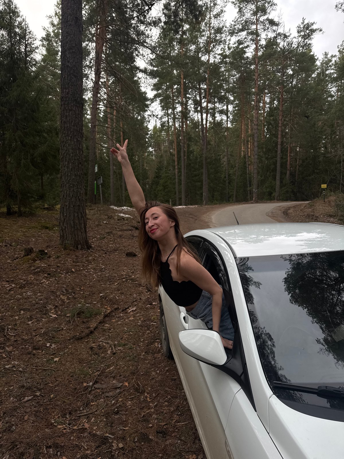 Woman poses playfully in car window during forest photoshoot