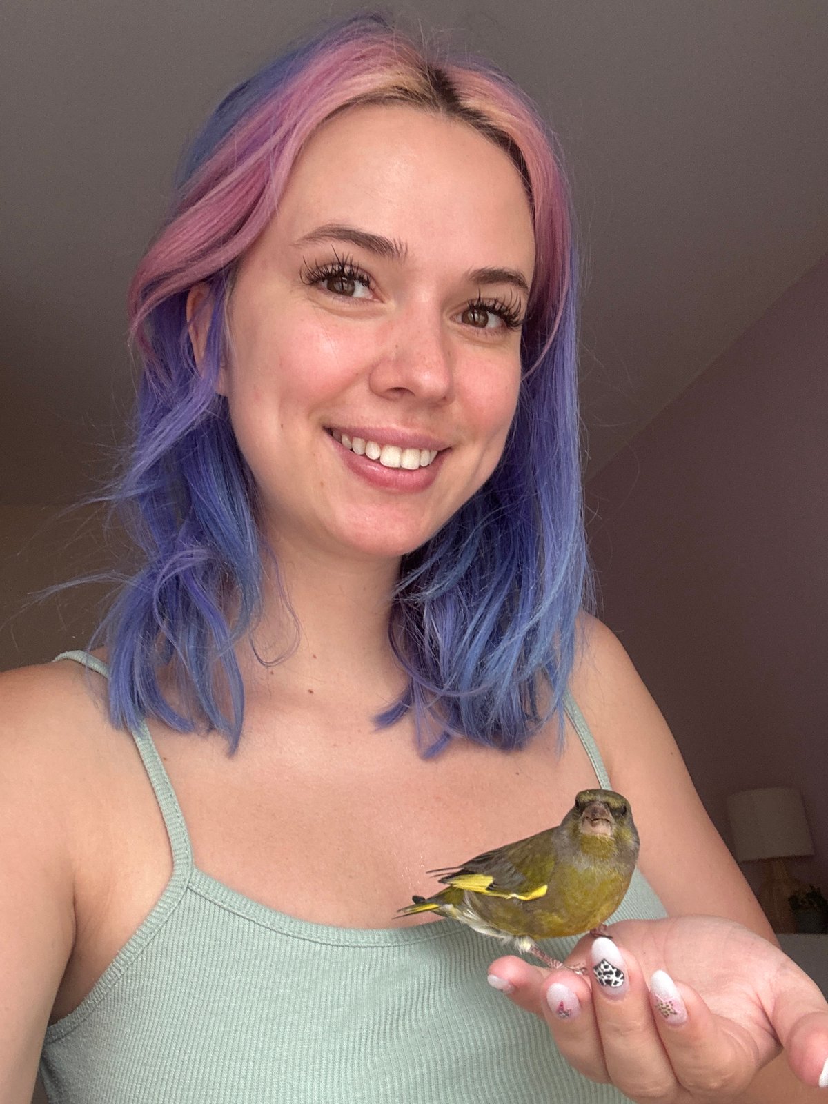 Woman with colorful hair poses with pet bird in Spain
