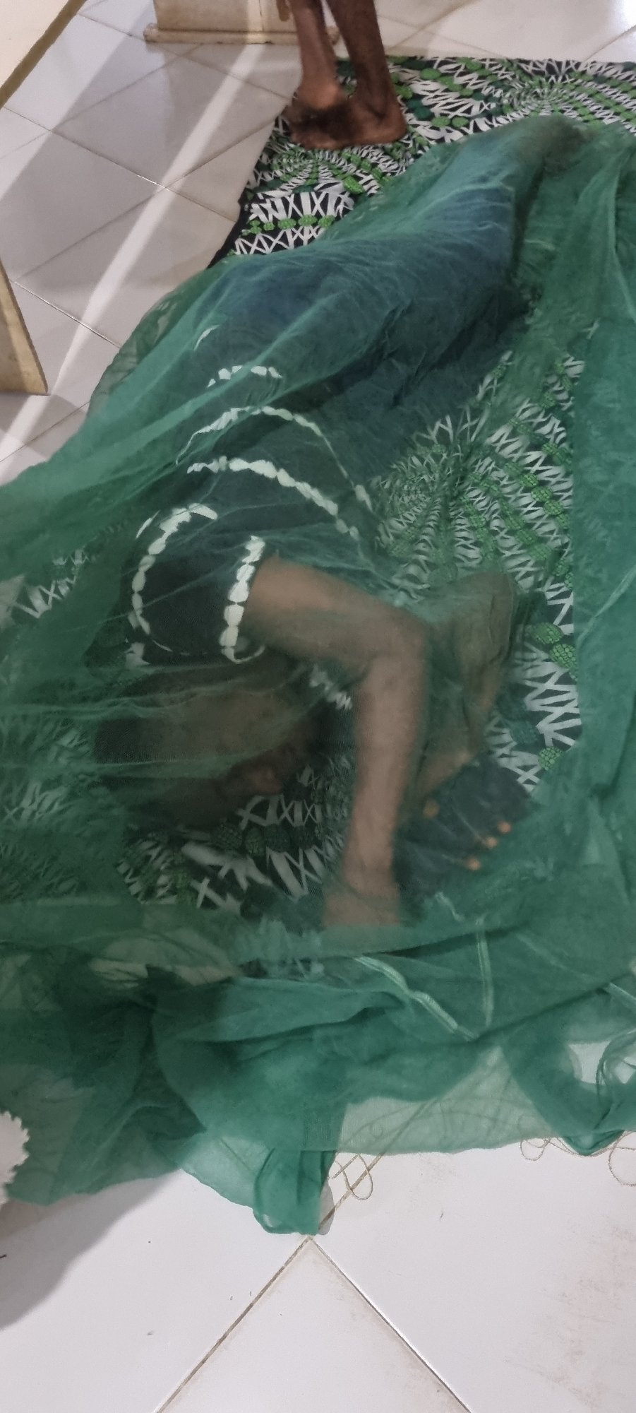 Resting under a green mosquito net indoors in Lagos