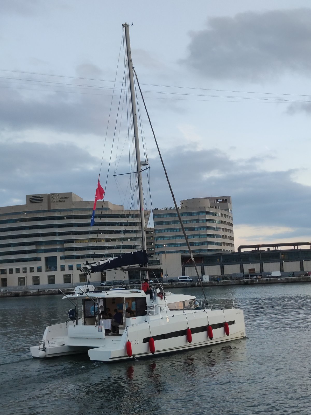 White catamaran sails Barcelona harbor at twilight