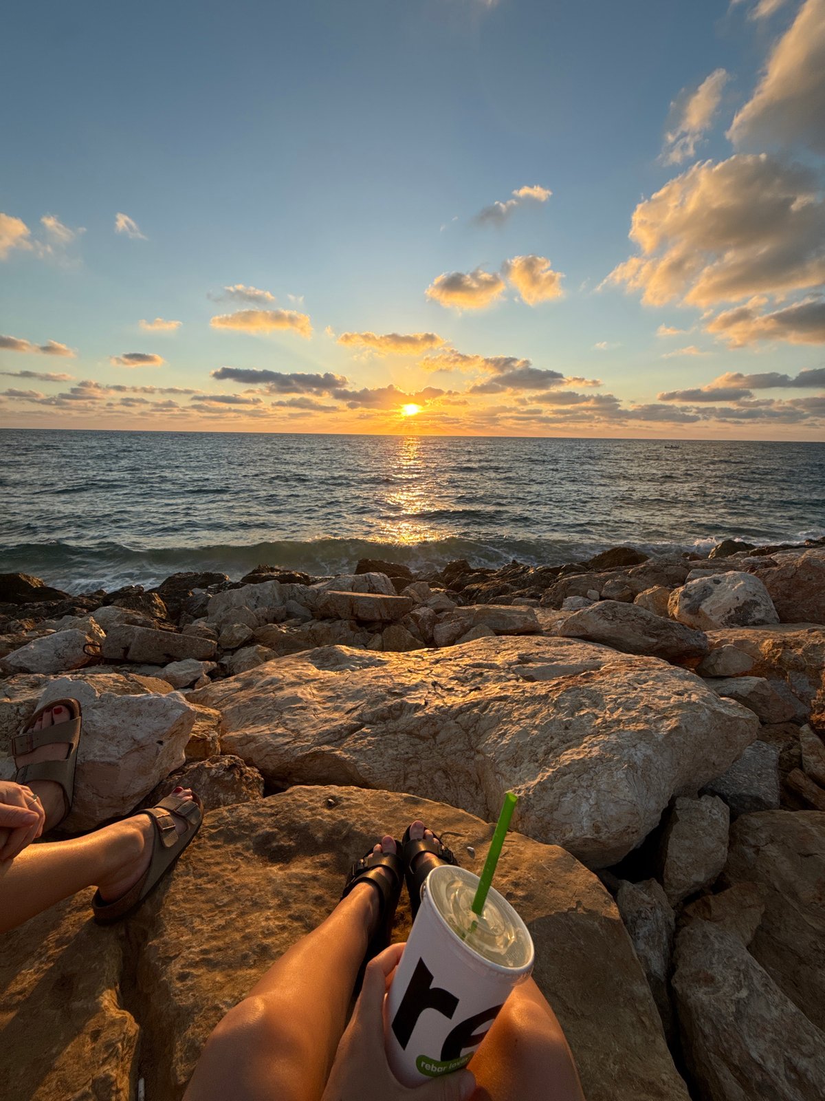 Drink in hand, feet up on the rocks by the Tel Aviv shore.