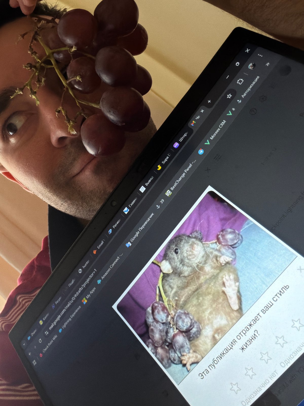 Man playfully balances grapes on forehead while using laptop