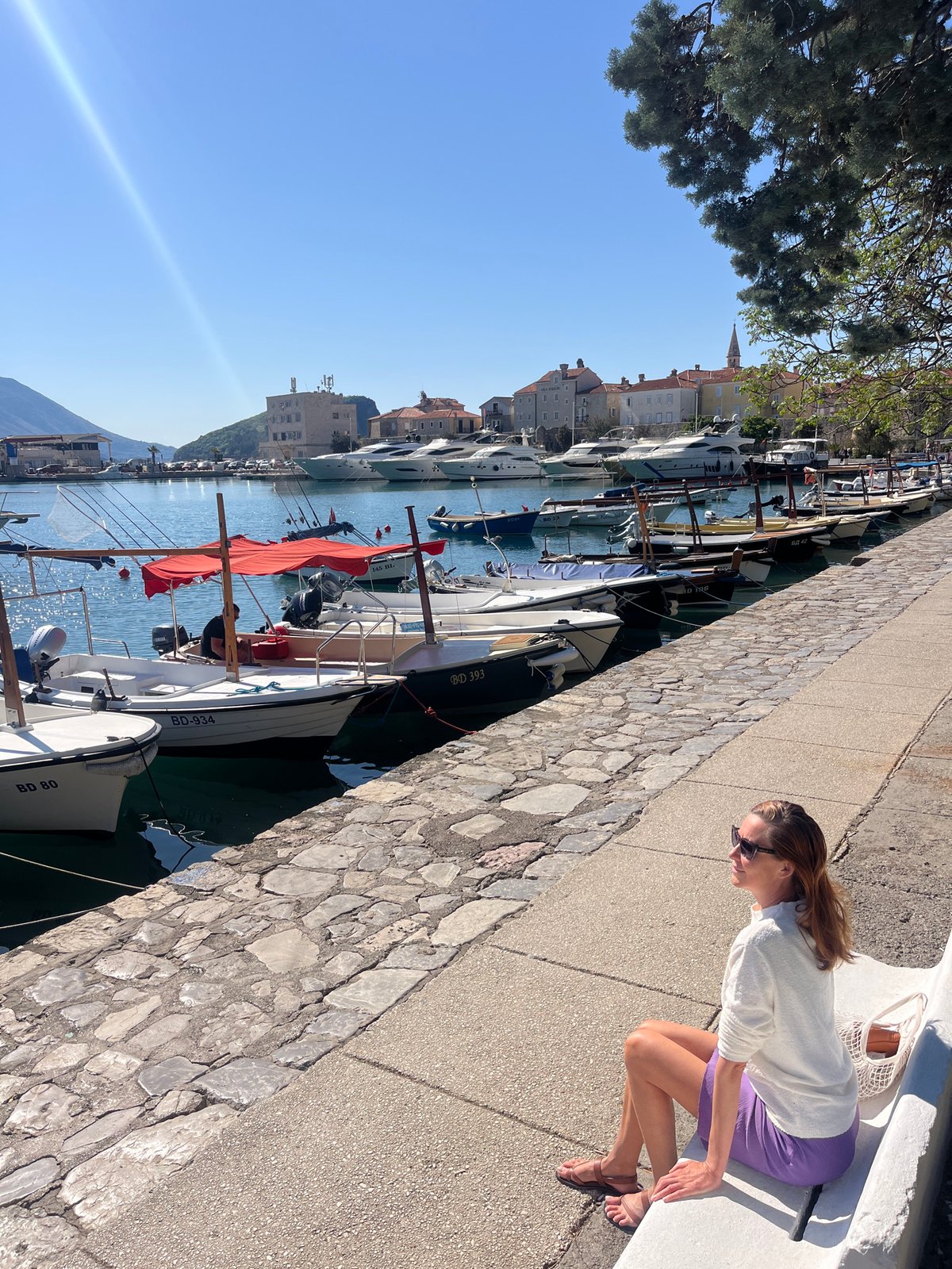 Woman in purple skirt strolls Budva waterfront, watches boats and ducks