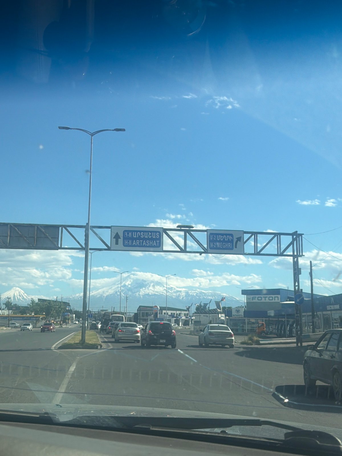 Highway traffic flows toward snow-capped mountains under cloudy skies