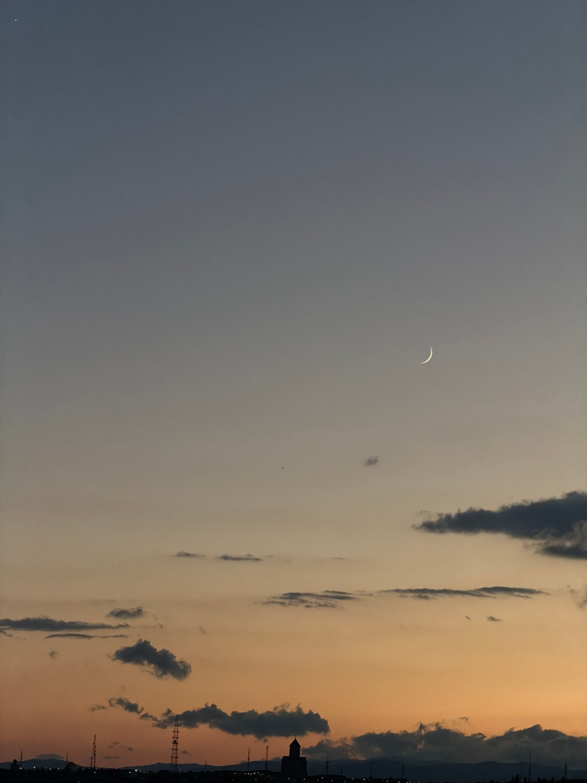 Crescent moon rising over Tbilisi on a cloudy evening