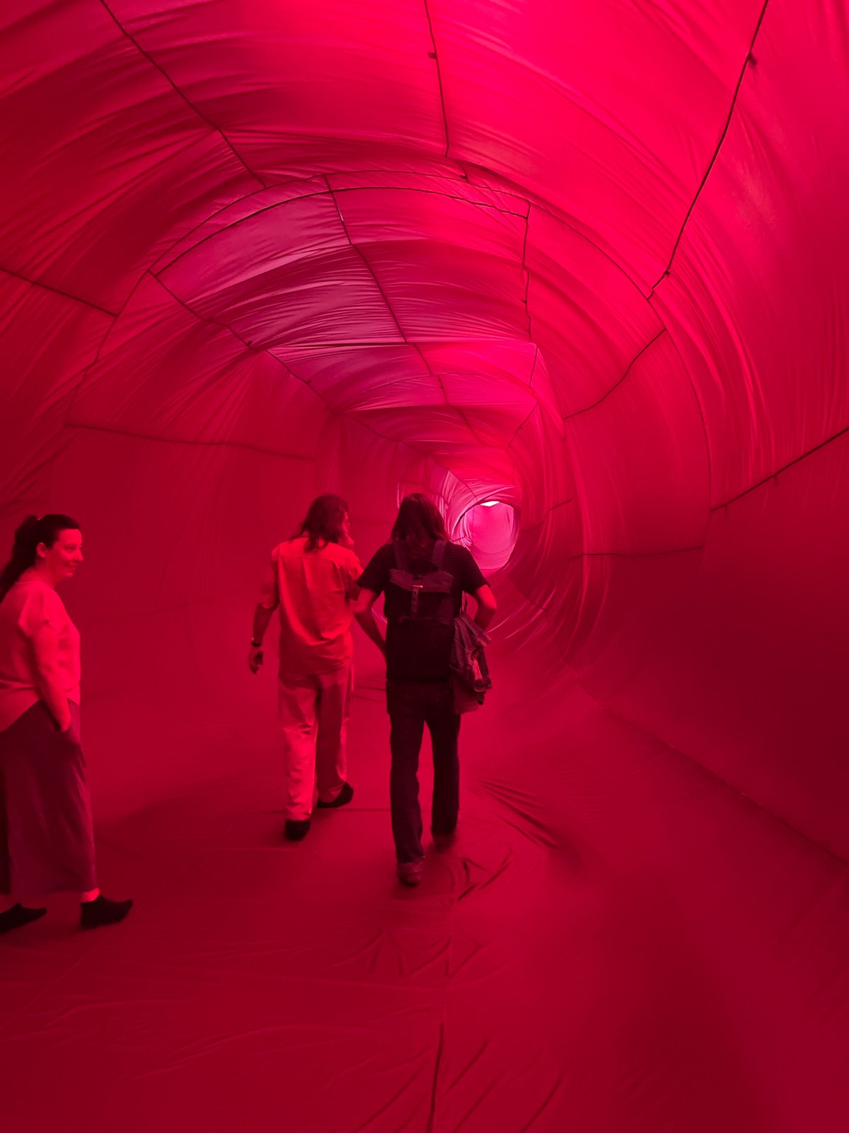 Three people explore illuminated red tunnel structure in Mexico City
