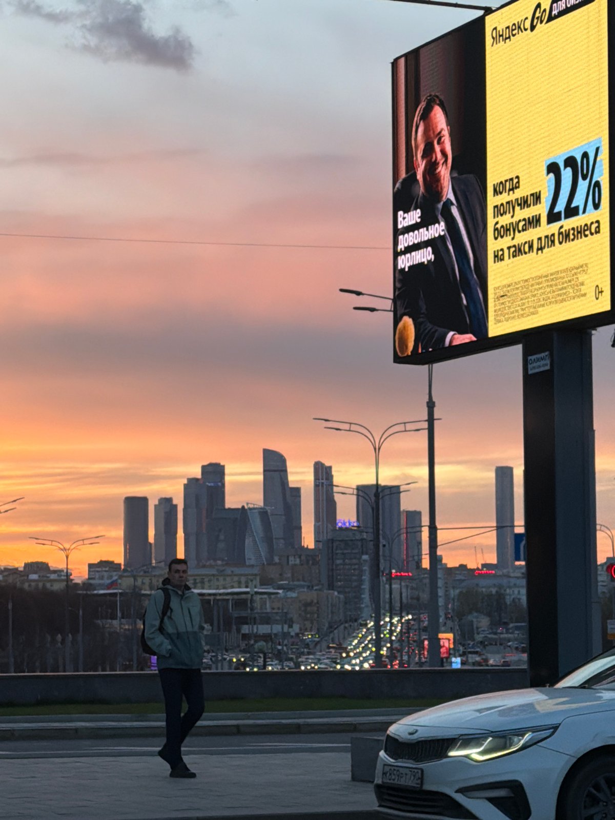 Pedestrian walks Moscow street at sunset near city skyscrapers