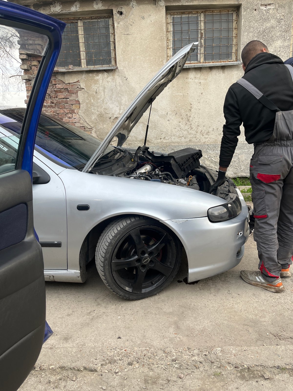 Man repairs damaged silver car in Pleven, Bulgaria