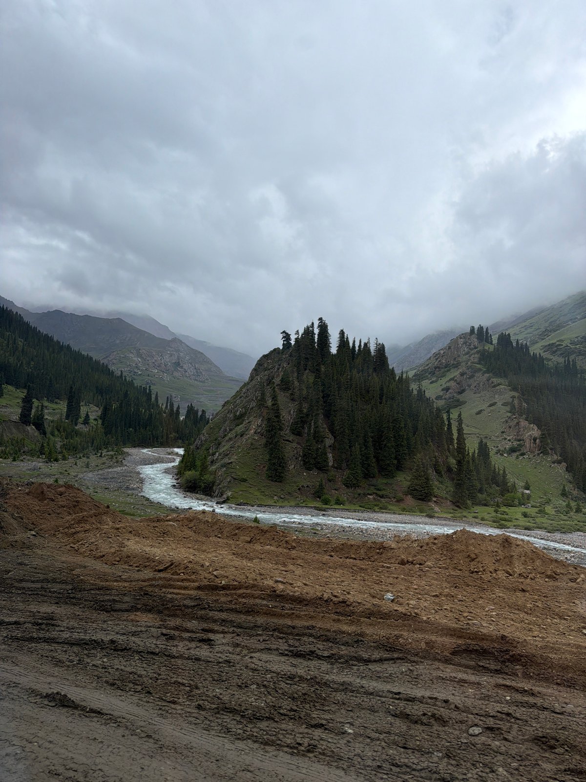 White-water river winds through a forested Kyrgyz mountain valley