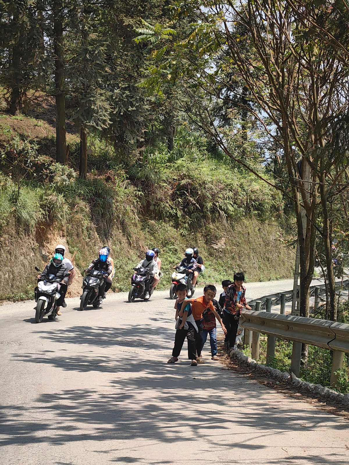 Motorcyclists travel mountain road past children in Vietnam commune