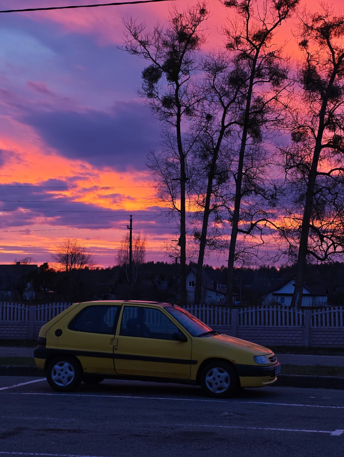 Yellow Citroen parked near residential fence under pink sky