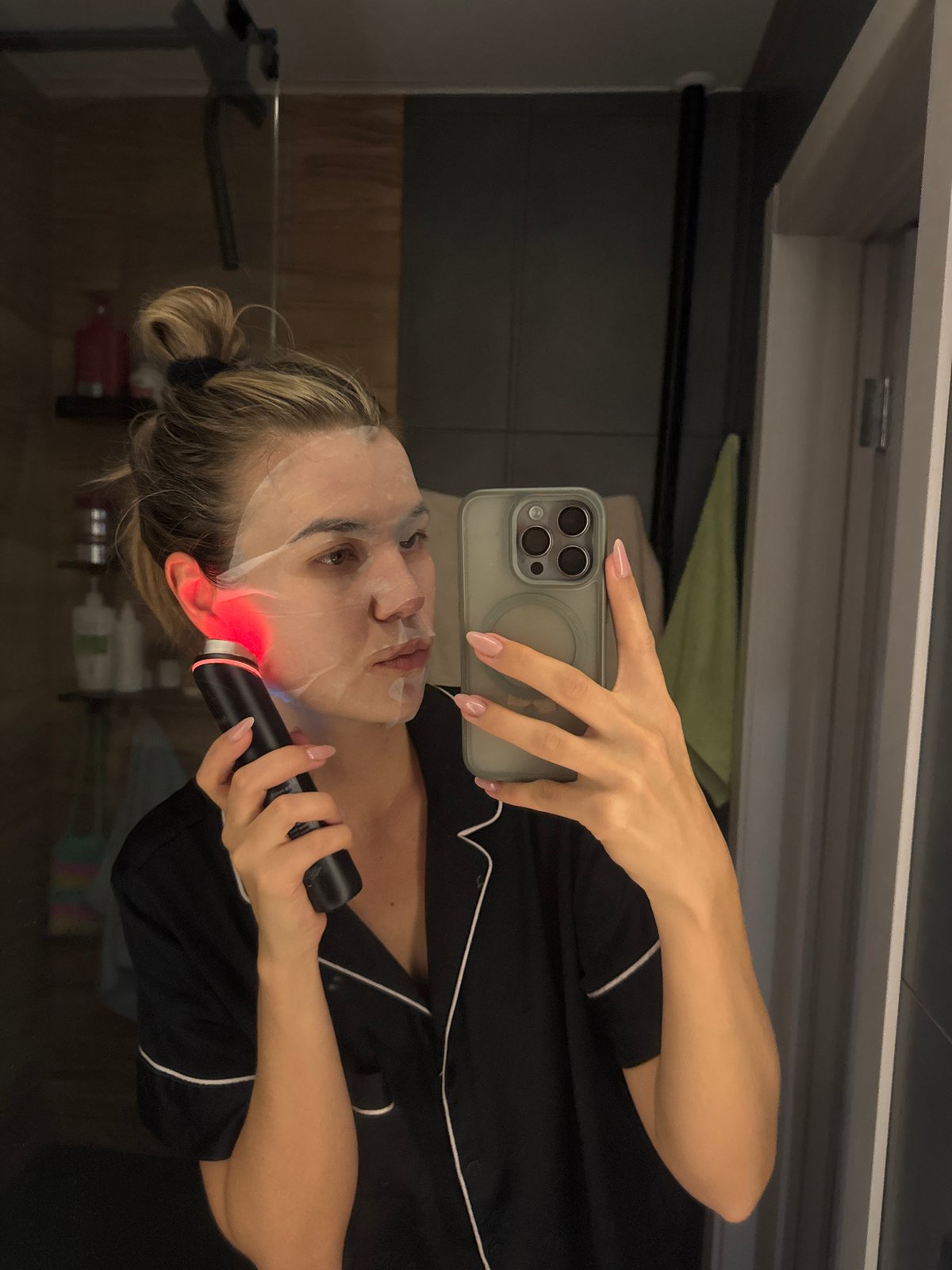 Woman takes selfie while using facial device in bathroom