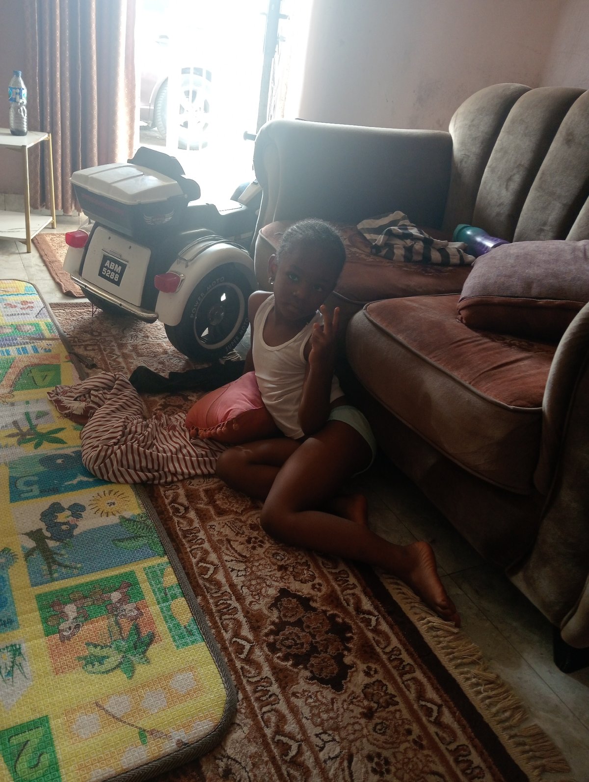 Child makes peace sign gesture on rug in Jos