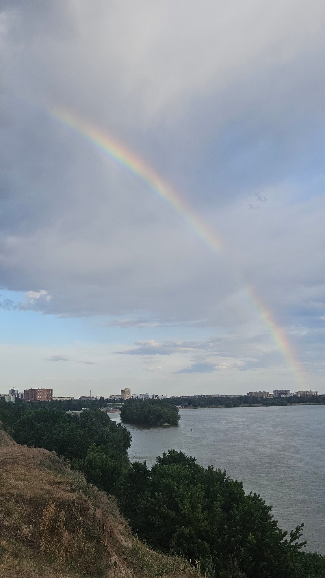 Rainbow over a wide river and metal bridge on a cloudy day