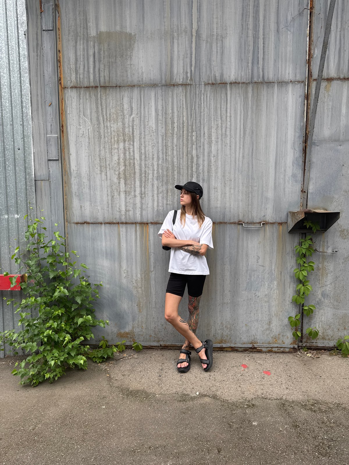 Tattooed figure poses against corrugated metal wall in Moscow
