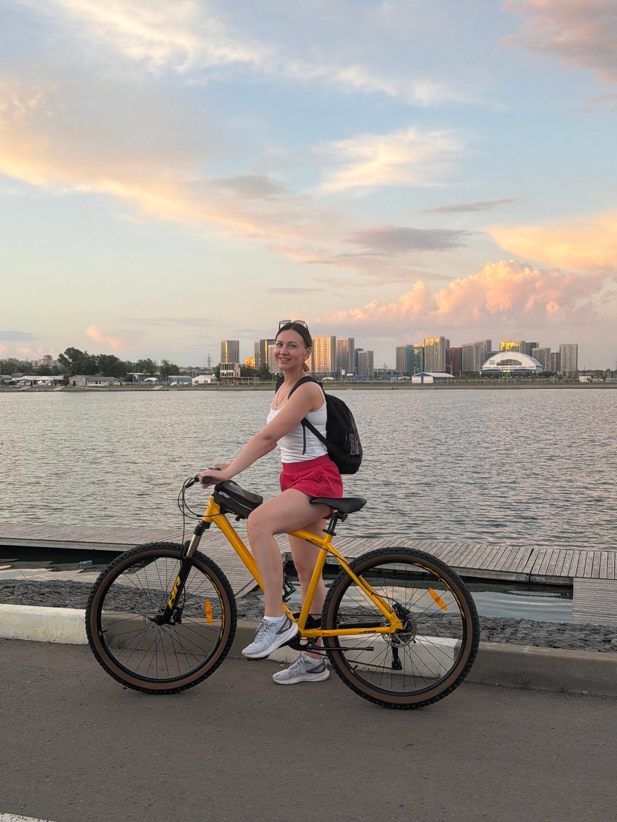 Woman poses with bicycle at waterfront during sunset rowing practice