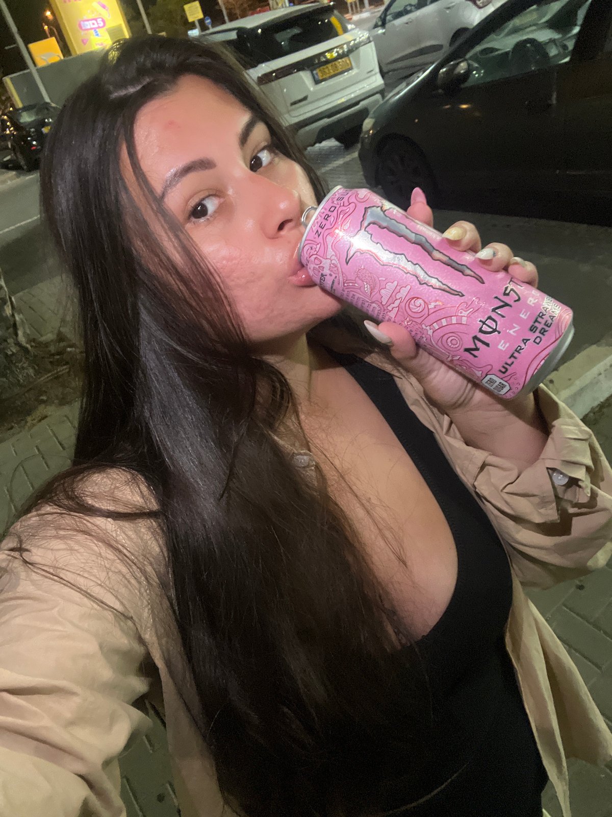 Woman refuels car while drinking energy drink in Kiryat Motzkin