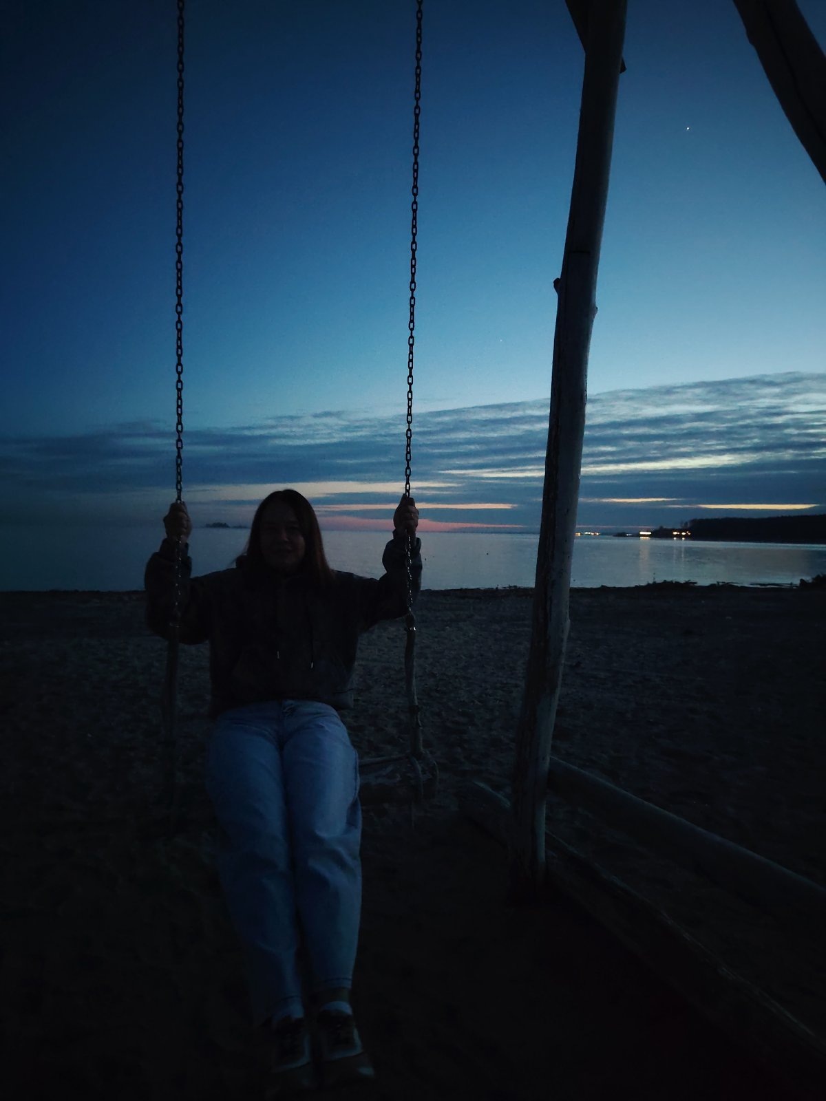 Person swings at beach during dusk hours