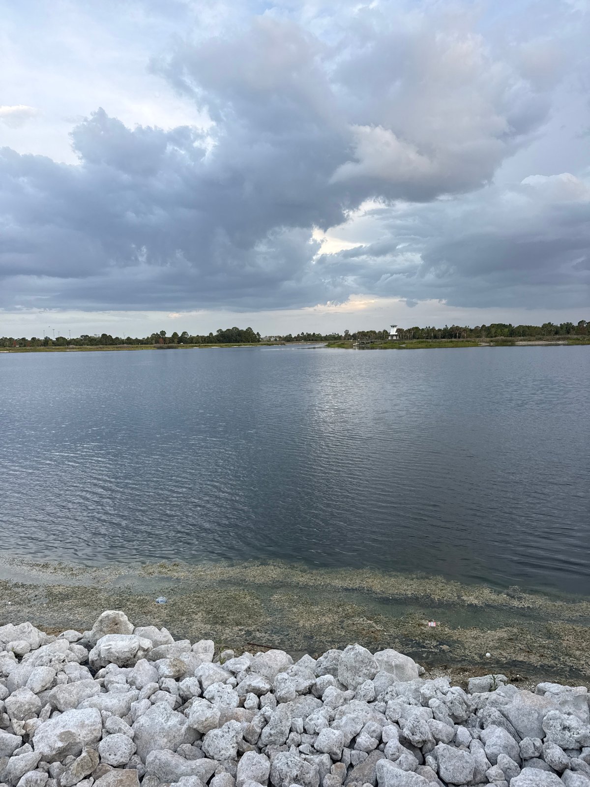 Calm waterfront park at dusk, rocky shore and outdoor dining nearby