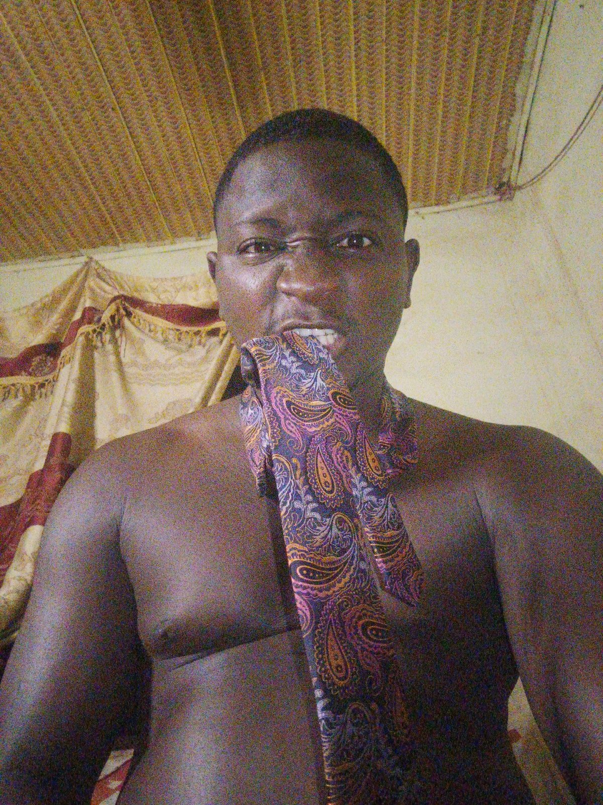 Man poses shirtless with colorful tie in Akwanga selfie session