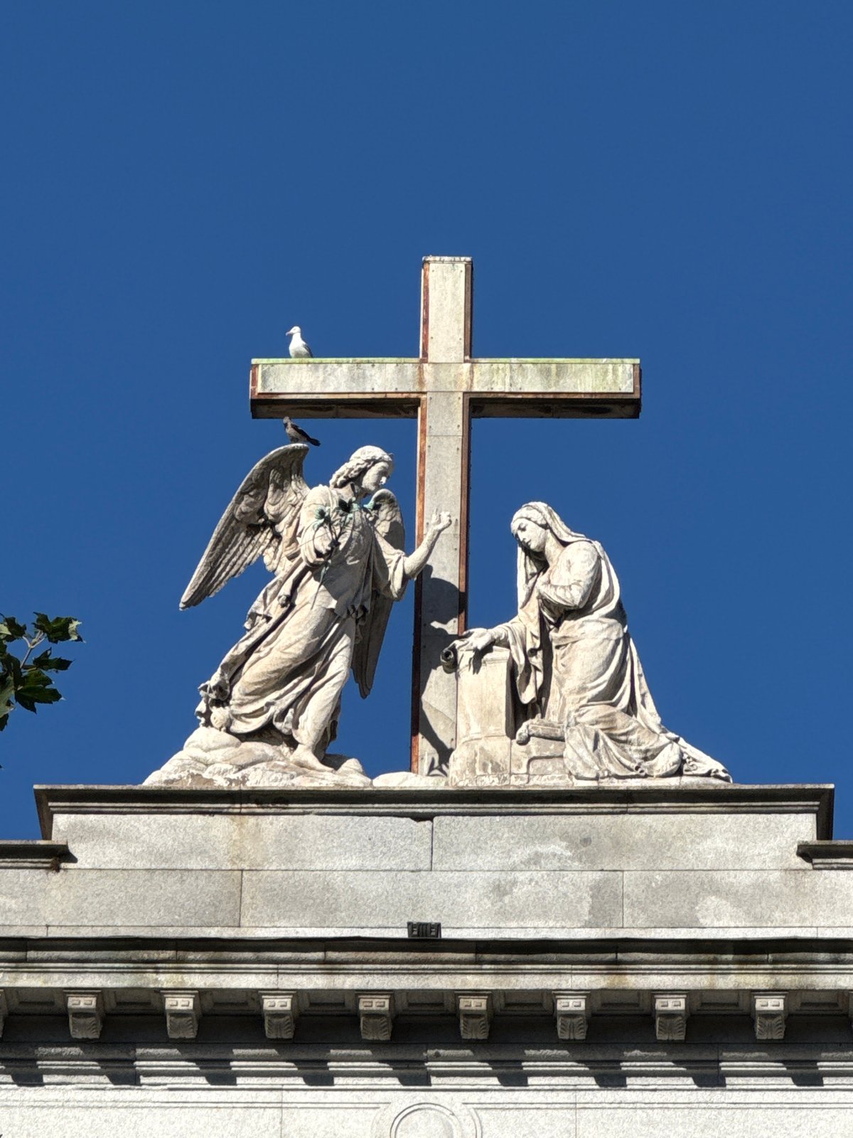 Weathered stone cross and angel sculpture on a Como rooftop