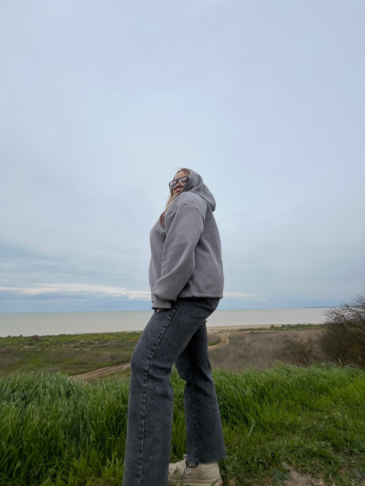 Woman in gray hoodie photographed at waterside in Port-Katon