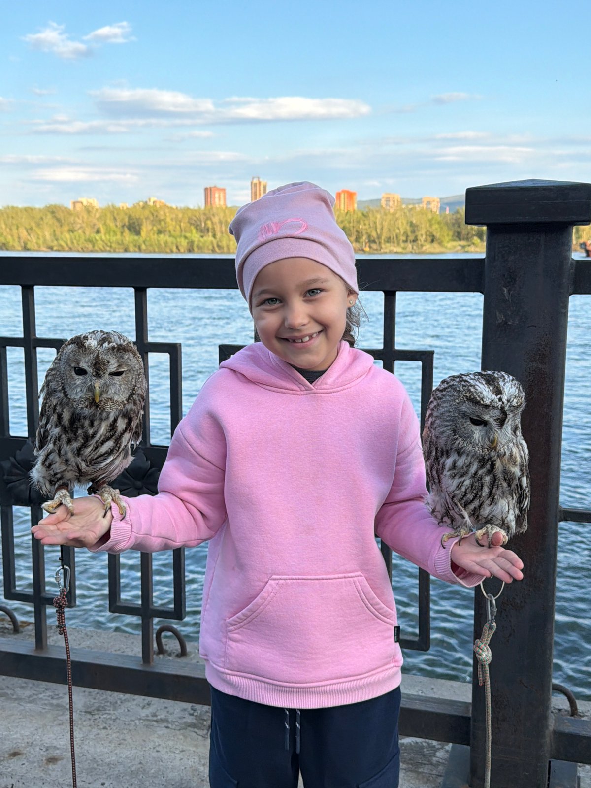 Girl poses with tethered owls on Krasnoyarsk waterfront pier