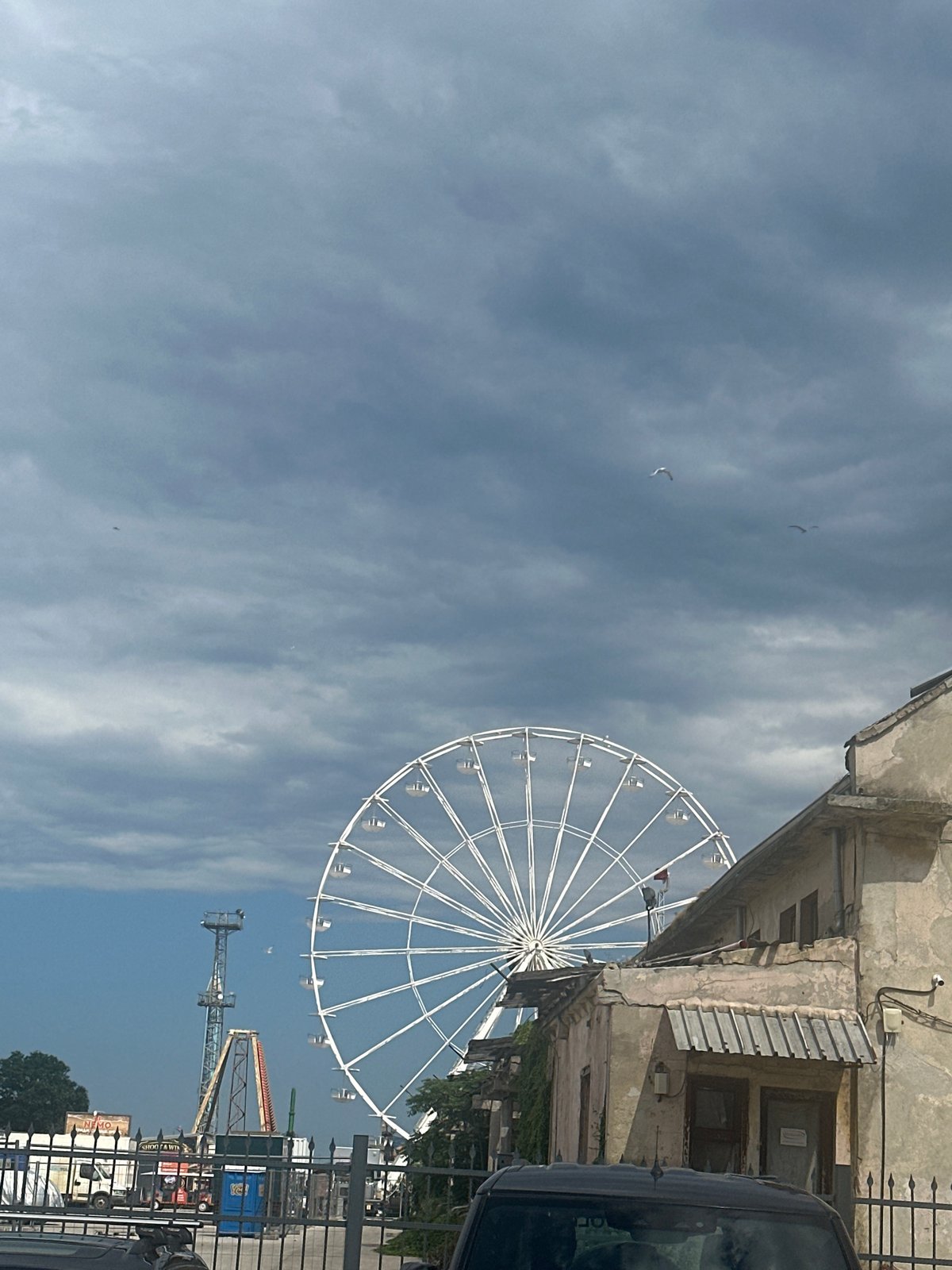 Derelict Ferris wheel beside a working port under stormy skies