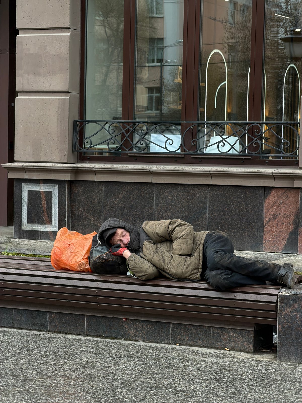 Man resting on urban bench with orange bag nearby