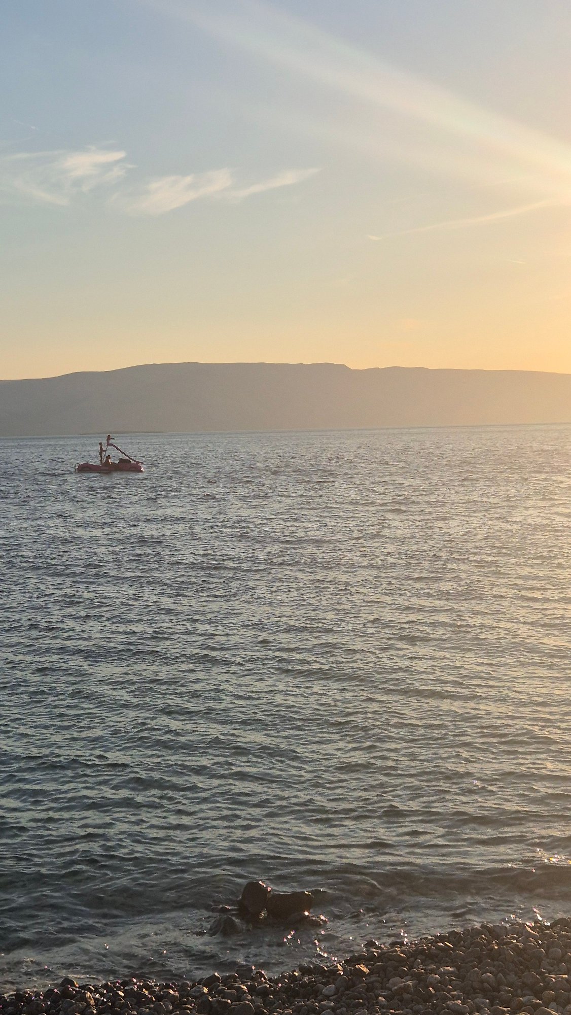 Red boat on calm water, misty mountains glowing in the distance