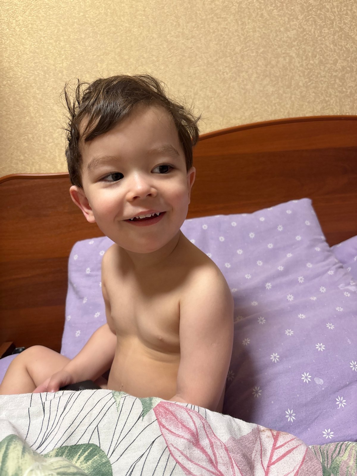 Child smiles while lying on floral bedsheets in Chaikovsky