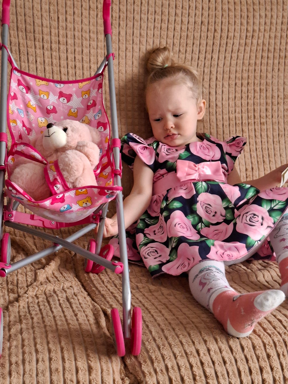 Child plays with toy stroller and teddy bear