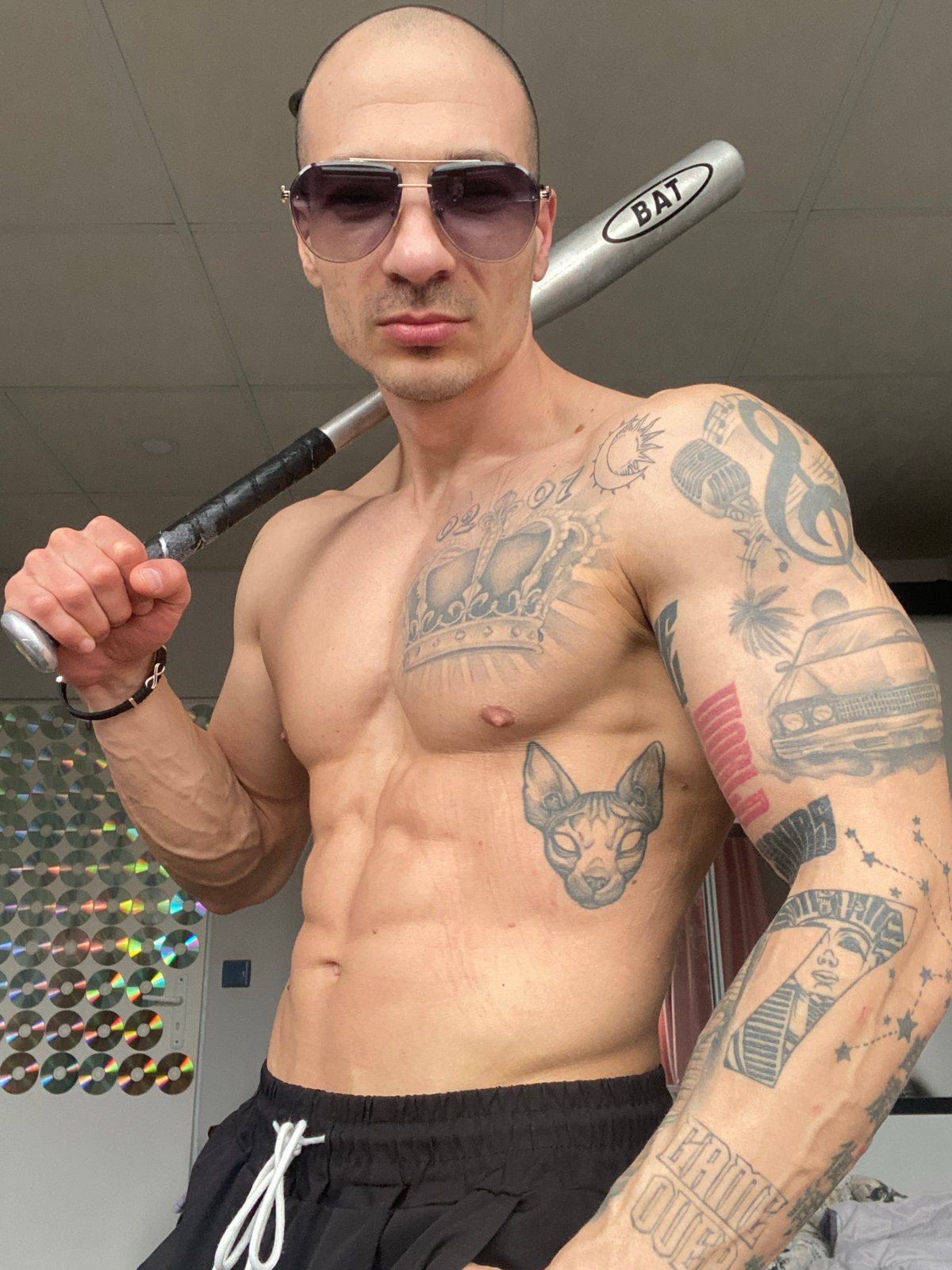 Man poses with baseball bat in CD-decorated room