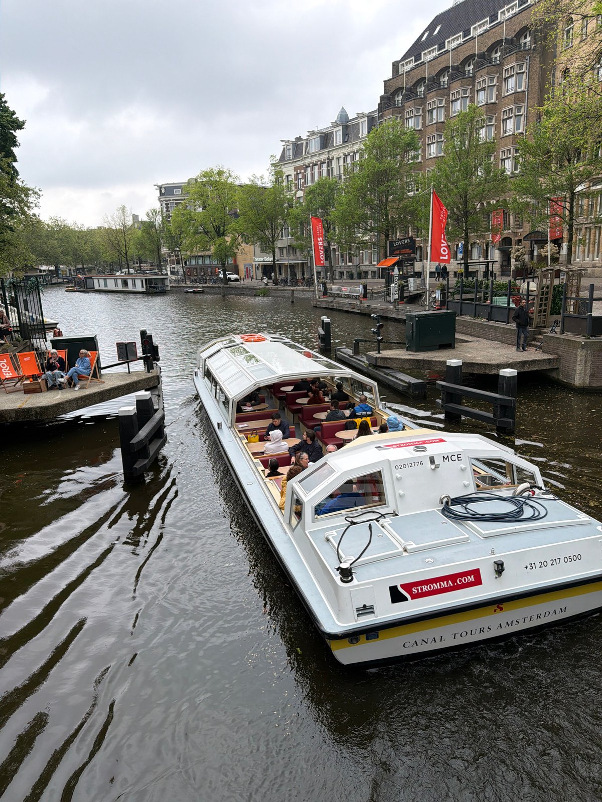 Tourist boat navigates Amsterdam canals past waterfront dining area