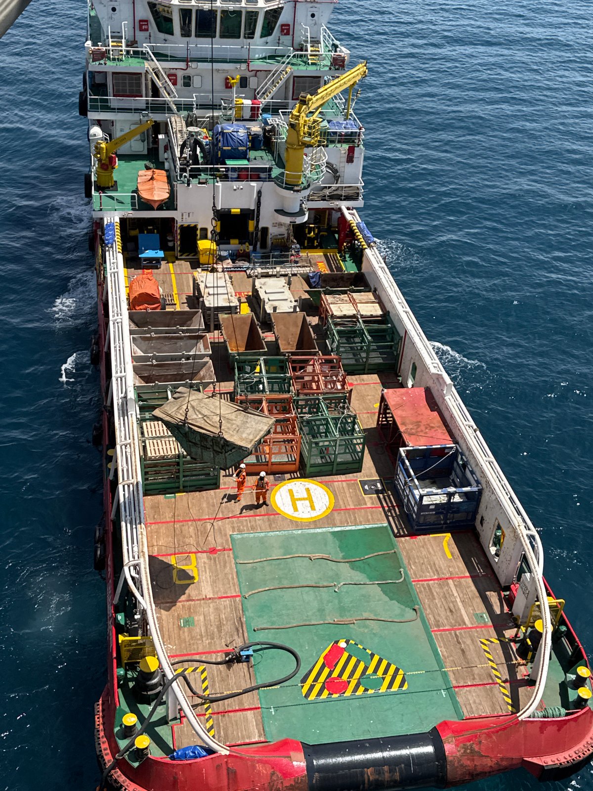 Offshore supply vessel at work, deck loaded, crew on the move
