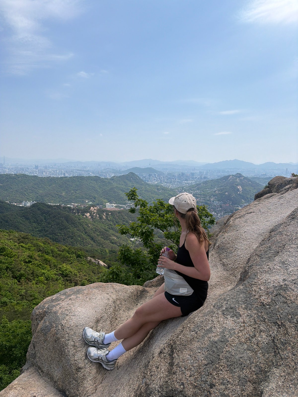 Early morning hiker surveys Seoul cityscape from mountain boulder