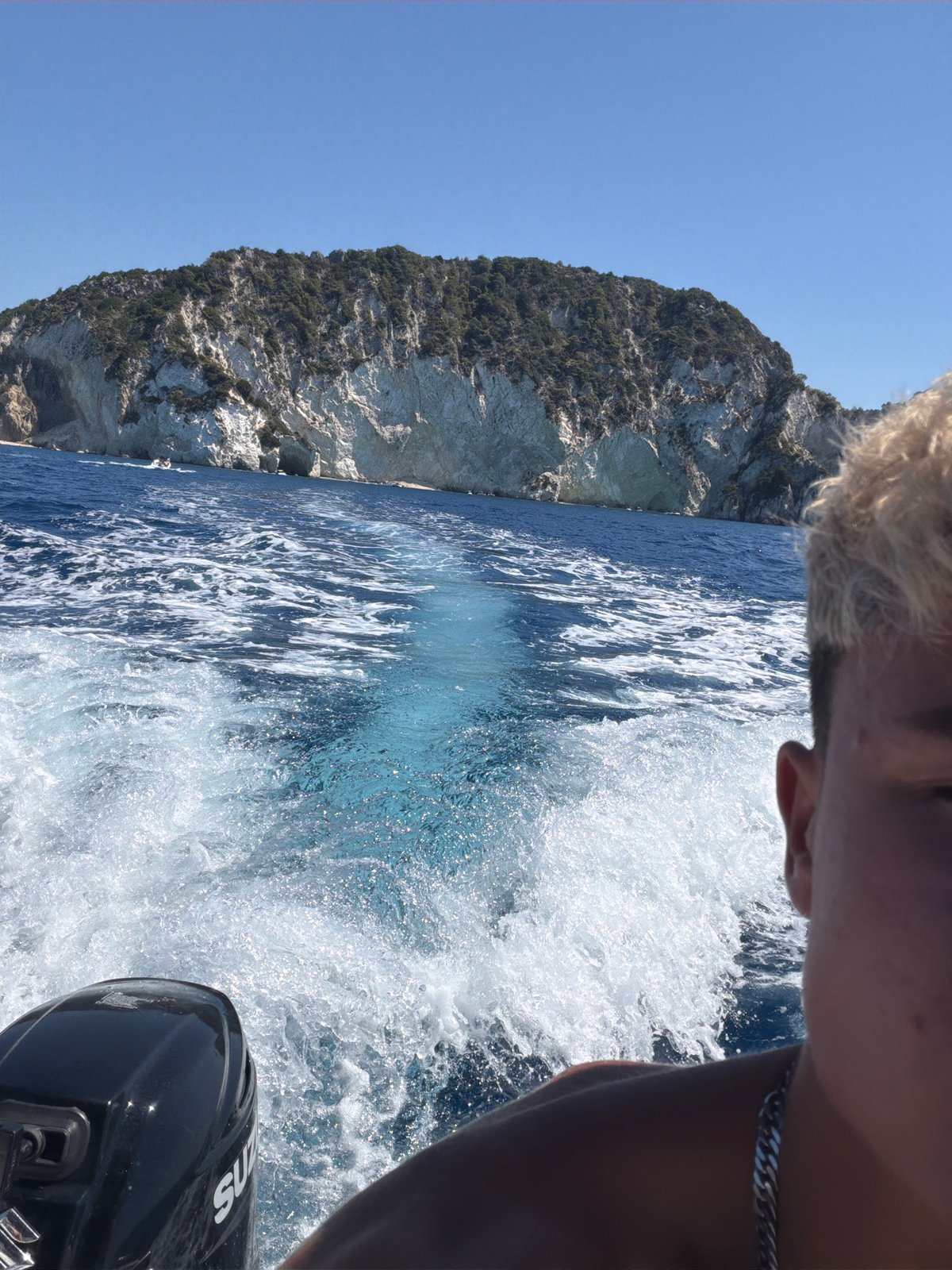 Boat cruising past a rocky island in open blue water