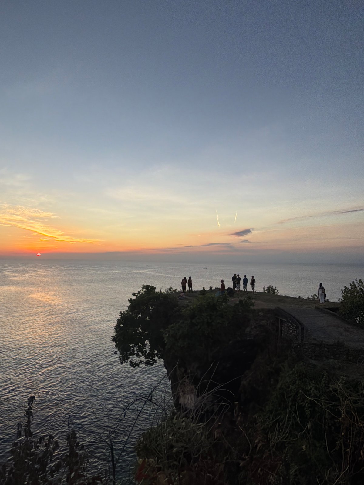 Cliff-side sunset watch over a calm tropical ocean