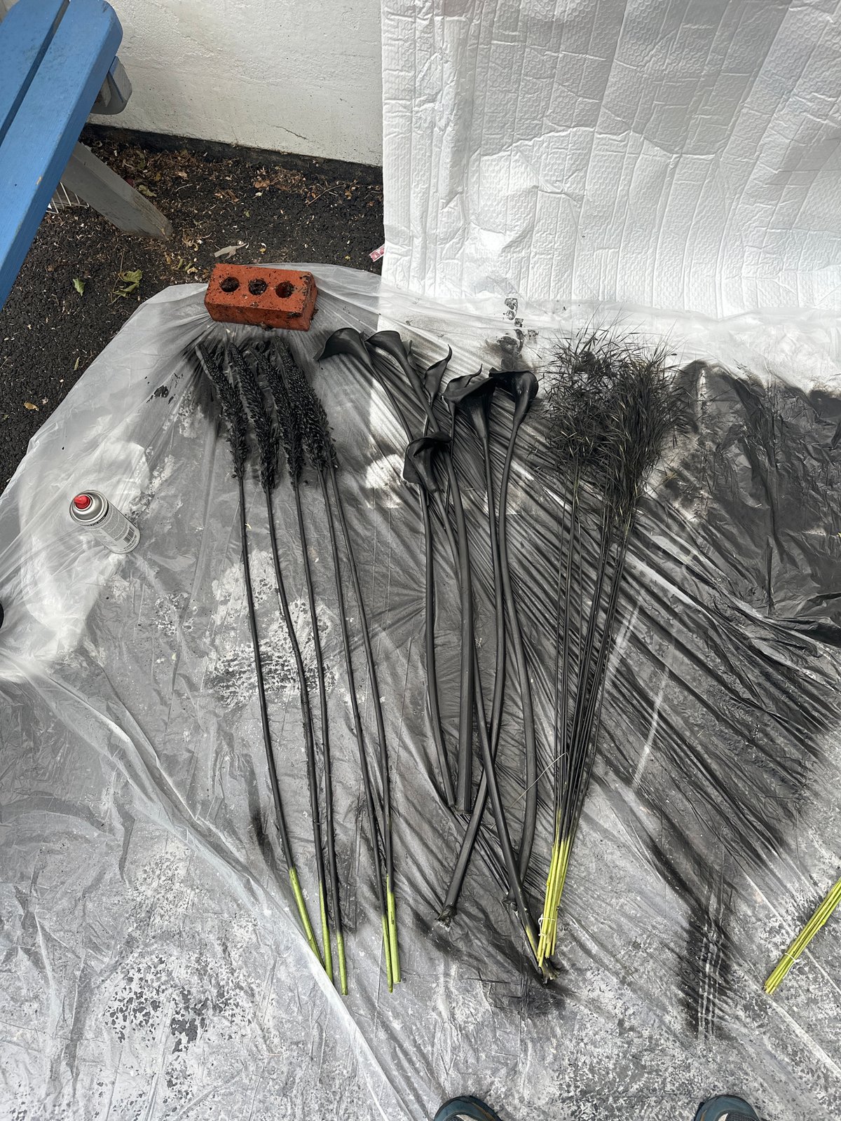 Artist spray-paints artificial flowers black in London outdoor workspace