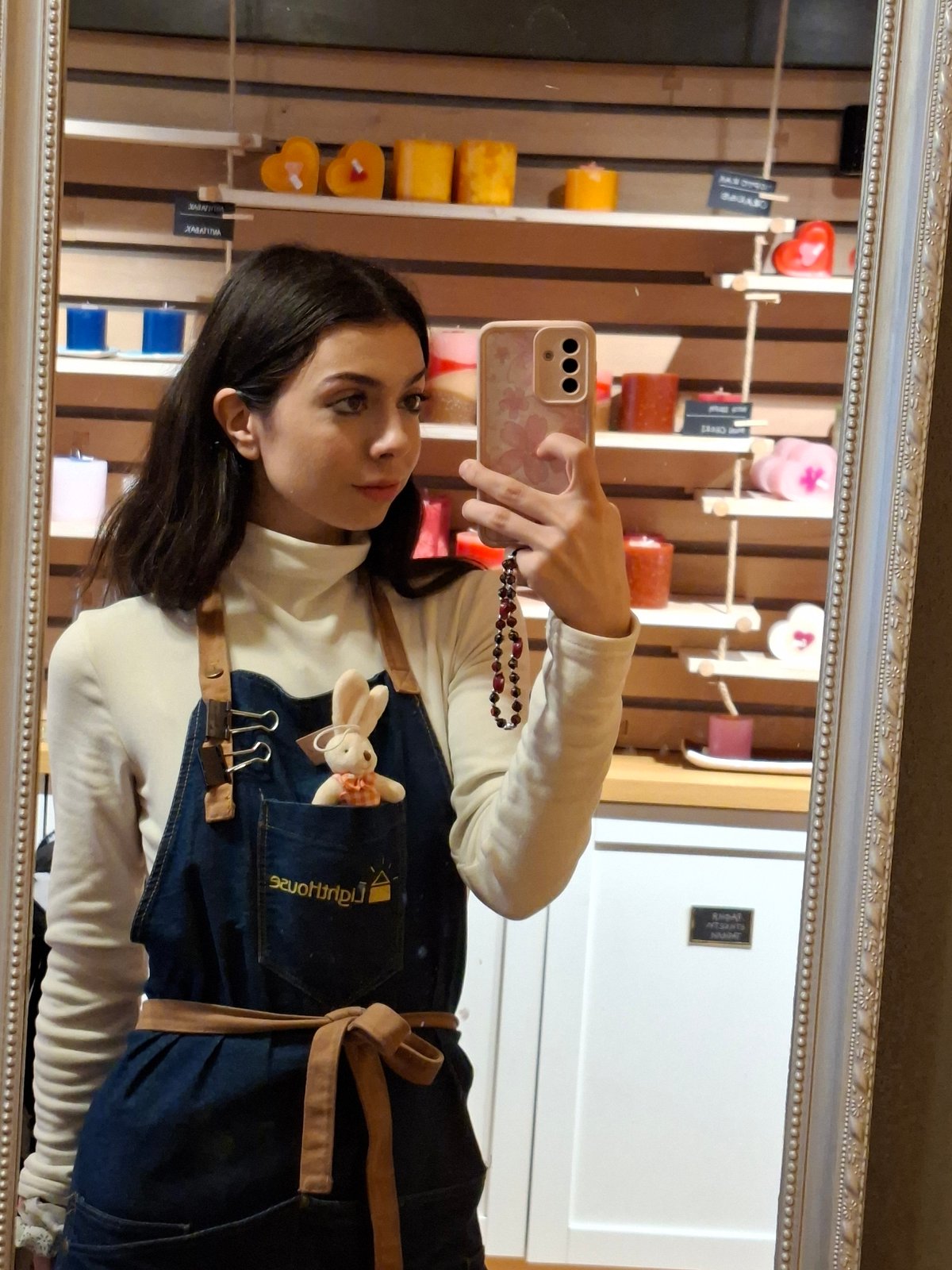 Woman poses in mirror wearing white sweater, denim apron