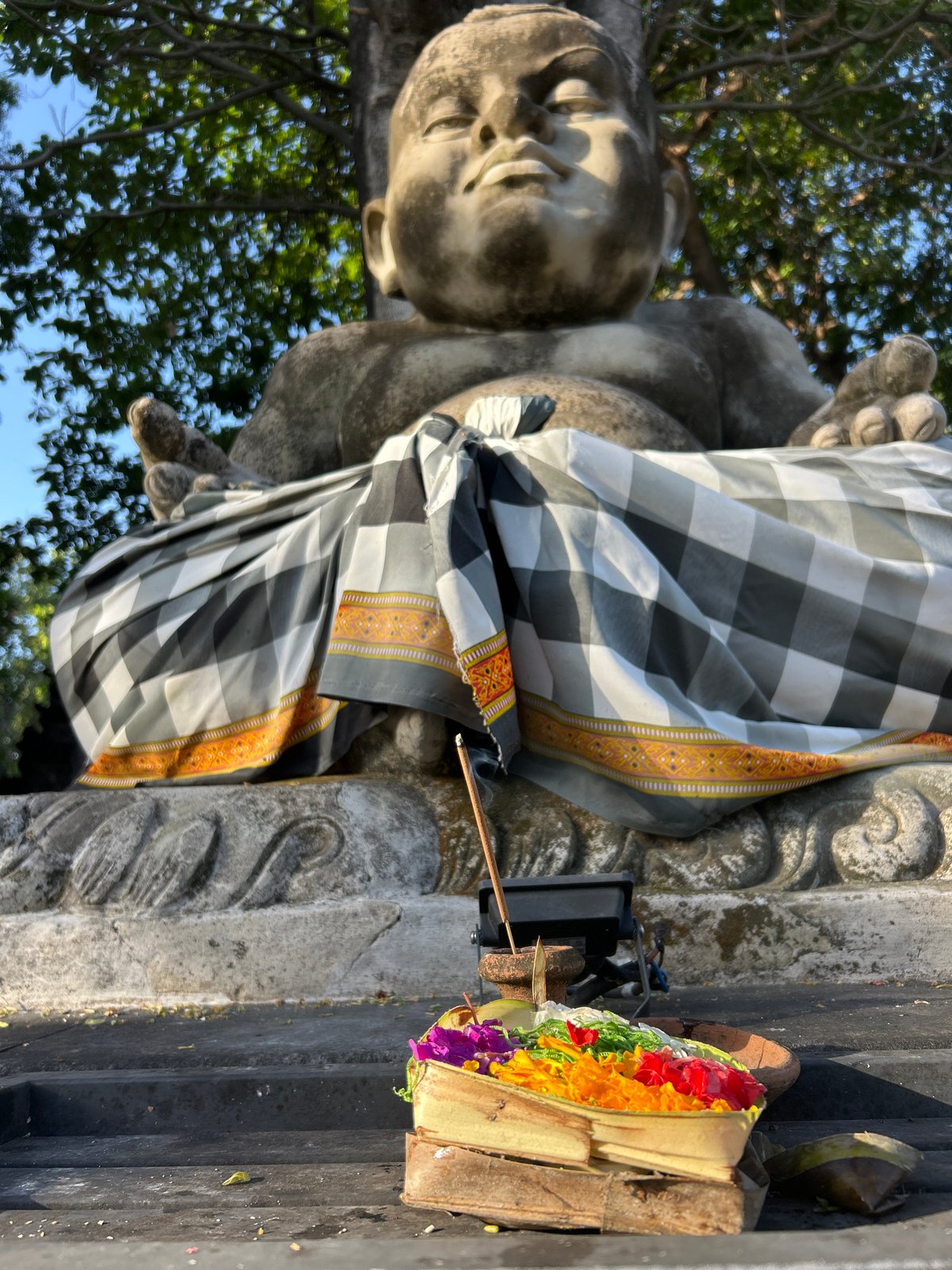 Balinese shrine statue with checkered sarong and offerings, Denpasar