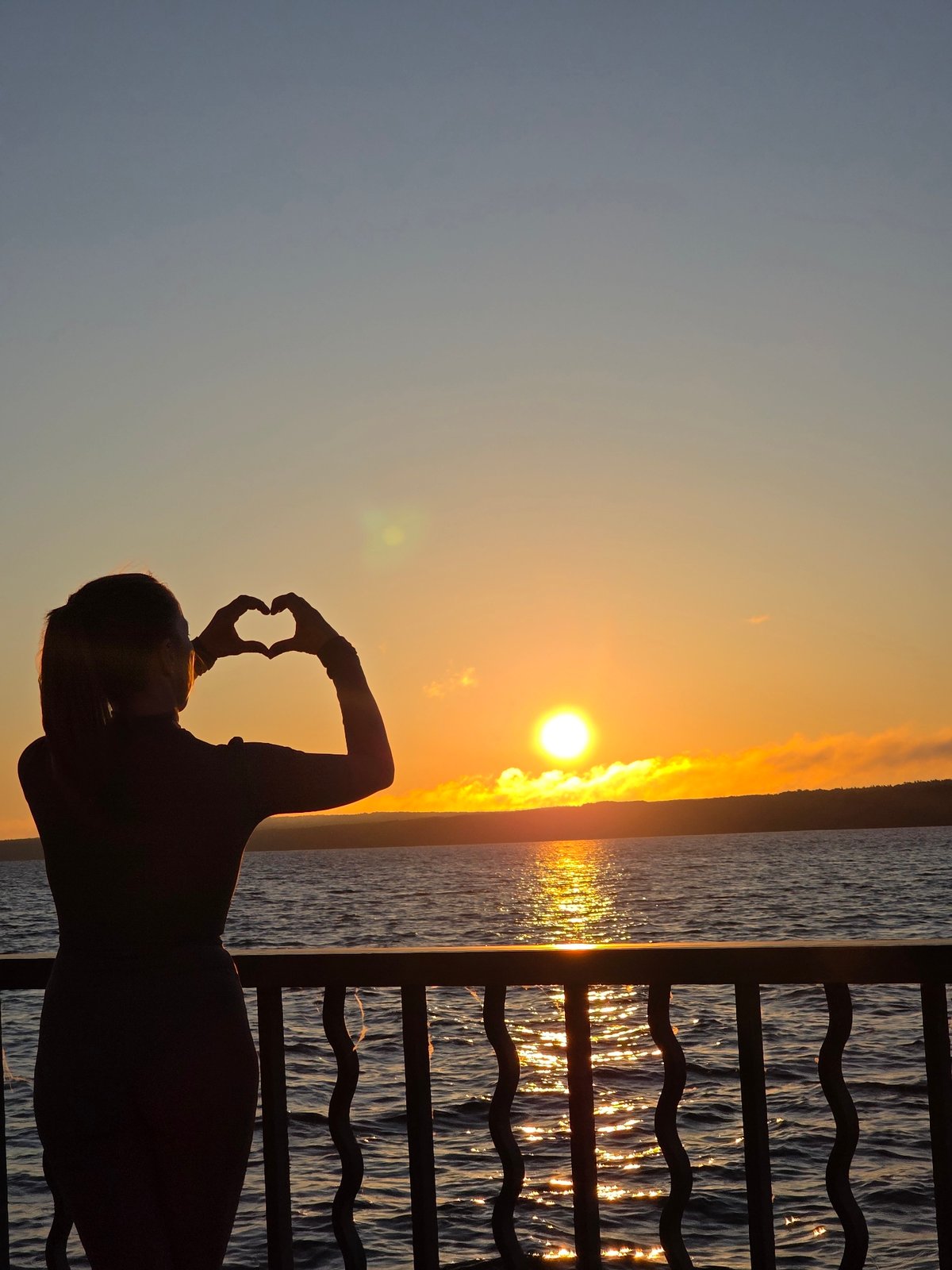 Person makes heart gesture on balcony during Chaikovsky sunset