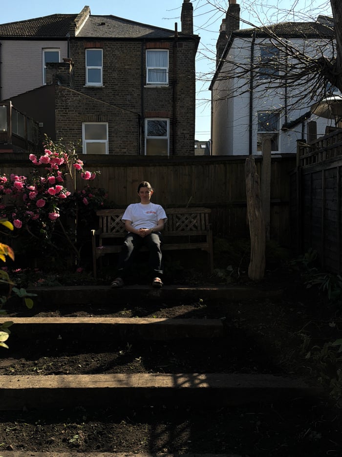 Person sits on garden bench in sunny London residential area