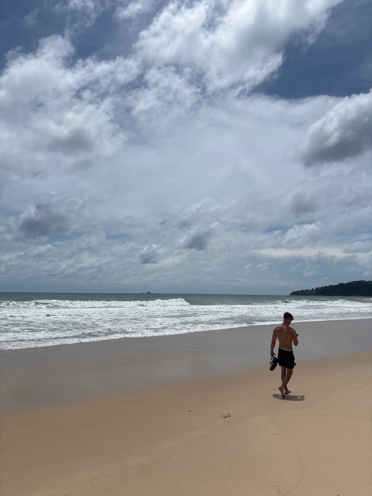 Man walks barefoot on Bang Tao beach, Thailand